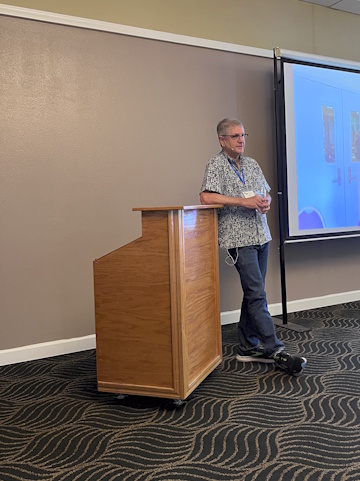 A man leans on the side of a podium next to a projector screen.